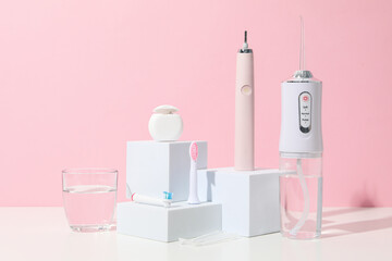 Electric toothbrush, irrigator and glass of water on pink background