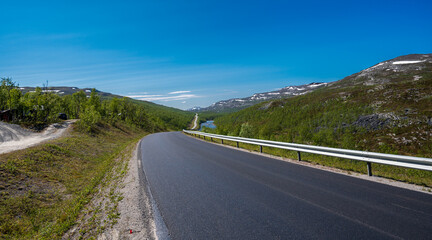 Asphalt road next to river with blue water in tundra