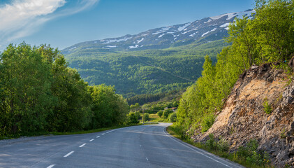 Winding asphalt road in green forest under high hill