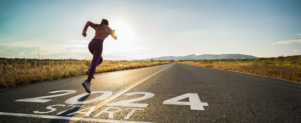 New year 2024 or start straight concept.word 2024 written on the asphalt road and athlete woman runner stretching leg preparing for new year at sunset.Concept of challenge or career path and change. - obrazy, fototapety, plakaty