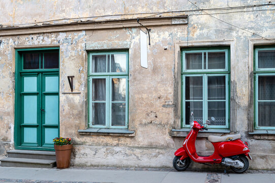 Red vintage scooter on the sidewalk in front of an old brick house