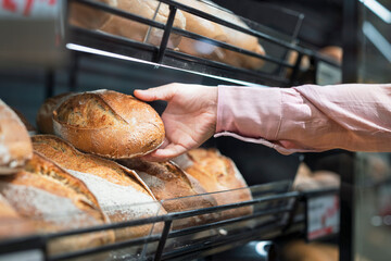 Close-up of man picking bread in bakery section of supermarket
