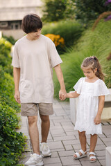 Adorable little girl walking in the park with her teenage brother. Happy kids 