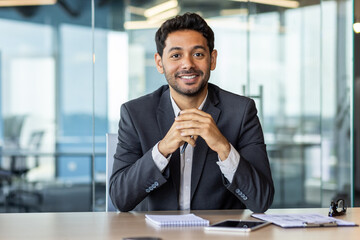 Portrait of young hispanic businessman inside office, boss in business suit smiling and looking at...