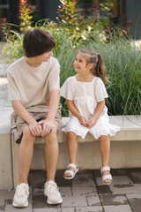 Adorable little girl sitting on bench with her teenage brother. Look to each other