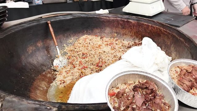 A large cauldron on a barbecue fire with Uzbek pilaf is cooked fried in oil Ingredients rice pepper lamb carrots garlic cumin coriander, at an open-air food festival.Concept Food Festival Central Asia