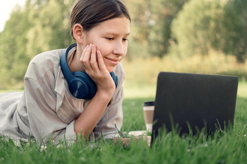 Teenage schoolgirl studying reading her books, tablet and notebook, sitting outdoors. Back to school. Student girl lying on the green grass using laptop in the college yard or park. Distance learning.