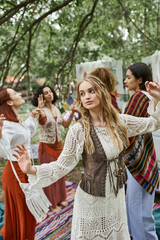 young blonde woman in boho outfit dancing near interracial friends in retreat center
