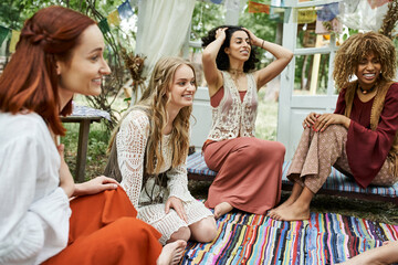 cheerful and multiethnic women in boho styled clothes talking outdoors in retreat center
