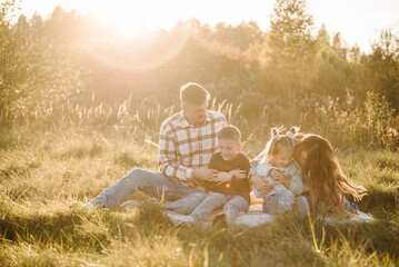 Mother, father, daughter, son sitting on blanket, hugging in grass in field at sunset. Family...