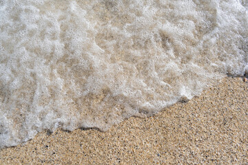 A soft wave runs on a sandy shore on a summer day. Empty space can be used as background for display or montage your top view products.