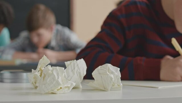 Closeup of crumpled paper sheets on desk in classroom with teenage students writing test in blurred background