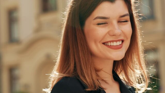 Portrait of young beautiful brunette woman wearing nice trendy black jacket. Sexy smiling model posing in the street at sunny day. Fashionable female outdoors with bright makeup