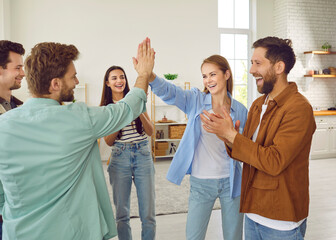 Portrait of a group of excited happy young friends students greeting each other giving high five when meet at home. Men and women standing in a circle enjoying time together at the party.