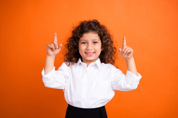 Portrait of charming cheerful schoolchild toothy smile indicate fingers up empty space ad isolated on orange color background