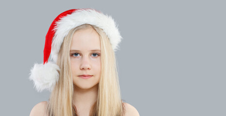 Portrait of pretty young blonde girl in Santa hat on gray background