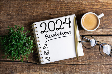 New year resolutions 2024 on desk. 2024 resolutions list with notebook, coffee cup on table. Goals,...