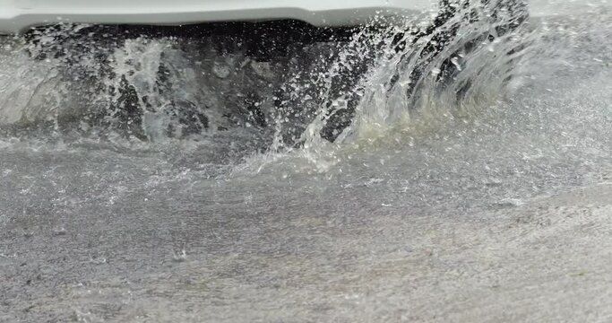 Very wet street in tropical rain, car passing and splash from the wheels, slow motion shot, lower view. Common weather at Ubud town in rainy season, some small roads become flooded with water