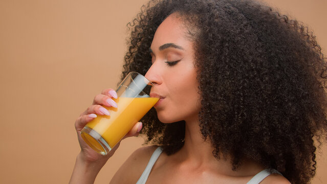 Beautiful happy healthy African American woman ethnic girl female model with curly hair drinking fresh orange juice vitamin drink diet detox organic vegetarian health care smiling in studio background