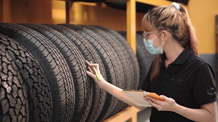 Worker young asia woman wearing face medical mask is checking quality of car tires and checking the...