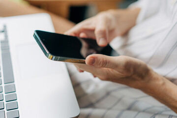 Close-up of a mobile phone in the hands of a woman. Woman uses phone and laptop for work.