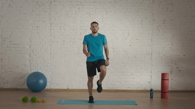 Man fitness coach in sportswear doing jumping cardio warm up for online class at the home studio.