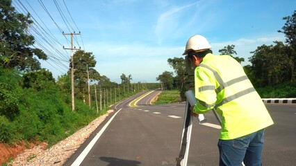 Surveyor engineer with theodolite on road highway during the sunny day with road in background..
