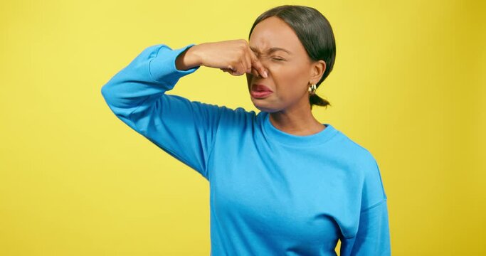 Beautiful young woman pinches nose smells bad odour stink, yellow studio
