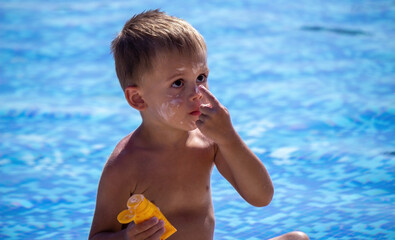 a boy in the pool smears himself with sun cream. Selective focus