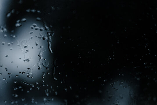 Regentropfen auf dunklem Glas bei Nacht