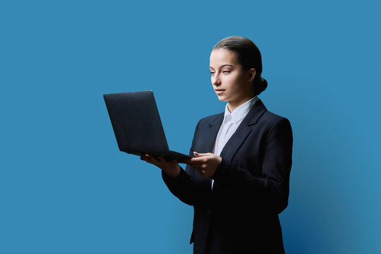 Serious teenage female student using laptop on blue background