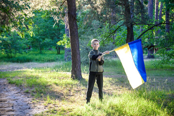 Ukrainian boy with waving flag and praying to stop the war in Ukraine in a field at sunset. War of...