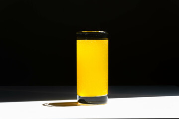 A glass of vitamin c water with bubbles on white table and black background