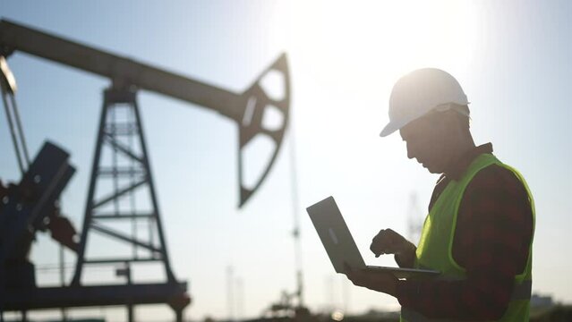 oil business. a worker works next to an oil pump holding a laptop. industry business lifestyle oil and gas concept. engineer studying the level of oil production on a laptop silhouette at sunset