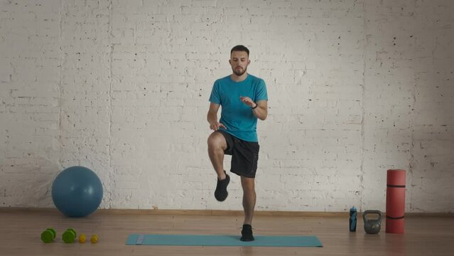 Man fitness coach in sportswear doing high knee jums in place warm up for online class at the home studio.