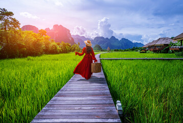 Asian woman walking on a wooden walkway with green rice fields in Vang Vieng, Laos