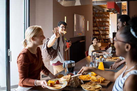 Diverse group of young roommates preparing and having breakfast together in their flatshare apartment