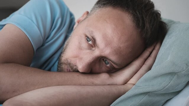 Man suffering from depression and life troubles loneliness on bed at home. Head on pillow close up. Insomnia, problems with sleep. Tired stressed person with Mental health disorder