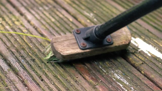 Cleaning old worn wooden decking with brush 