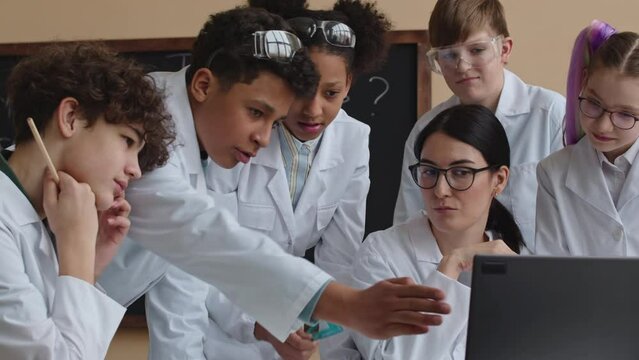 Medium shot of multiracial teenage school kids studying Chemistry with female teacher in modern classroom