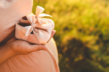 A pregnant woman holds cute baby shoes in her hands, the concept of expecting a baby