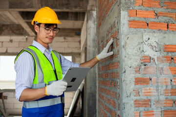A young Asian engineer wearing a safety vest uses a computer to check the construction history of a building. Construction engineer concept.