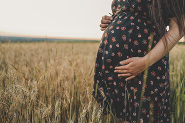 Close-up of pregnant woman with hands on her belly on nature background. Concept of pregnancy,...