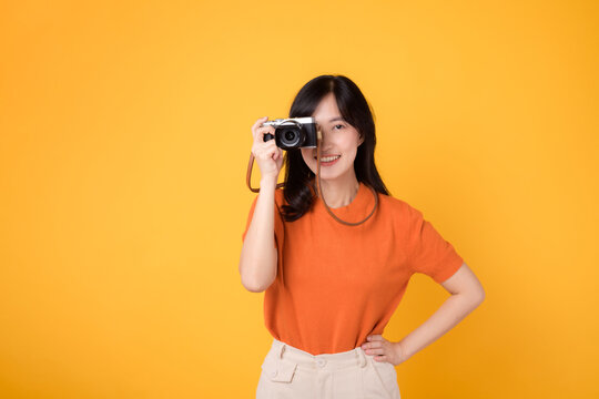 Vibrant woman with camera isolated on yellow background, showing the adventure of exploring new places on her vacation.
