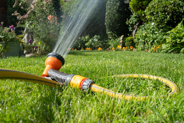 Shallow focus of an selectable generic garden sprinkler head seen showing a lush lawn during summer.