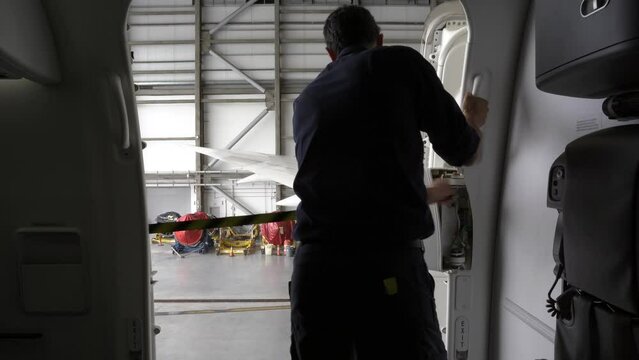 Male Latino Aircraft Technician closing a door on a commercial passenger airplane.