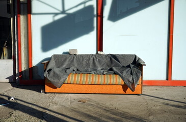 Altes ausrangiertes gestreiftes Sofa in Grün und Orange mit grauer Decke vor einem geschlossenen...