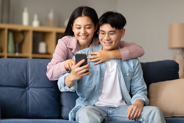 Obraz premium Korean couple sharing social media using smartphone gadget at home