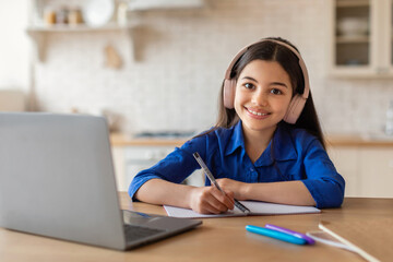 Happy arabic teenage girl in headphones sitting at laptop indoors