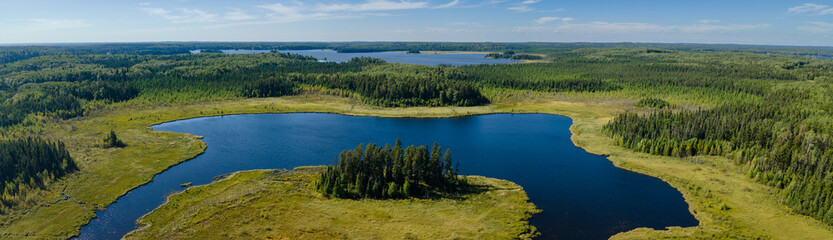 Naklejka premium Panoramic aerial view of a horseshoe shaped lake that is surrounded by an endless forest of evergreen trees. The blue sky has scattered white clouds. 
